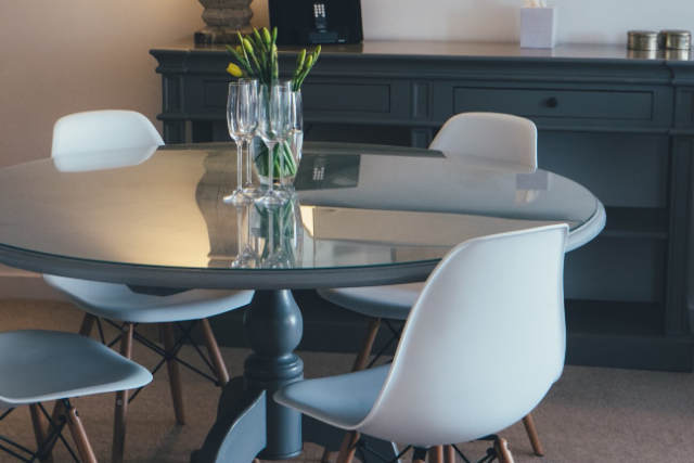 A round glass dining table with four white chairs.