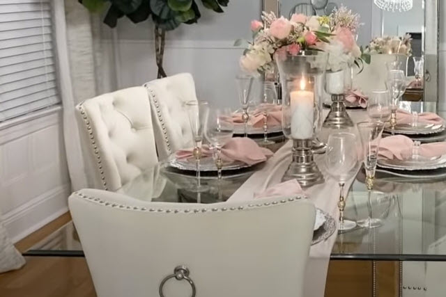 A white dining room with pink flowers and a glass table.