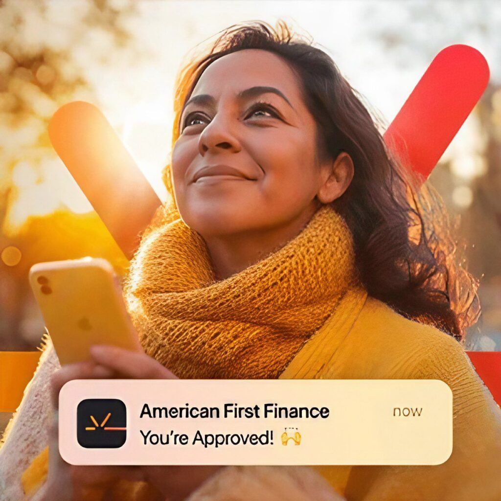 A woman in a yellow scarf holds a smartphone and smiles. A notification on her screen says "American First Finance: You’re Approved!" with a celebratory emoji.